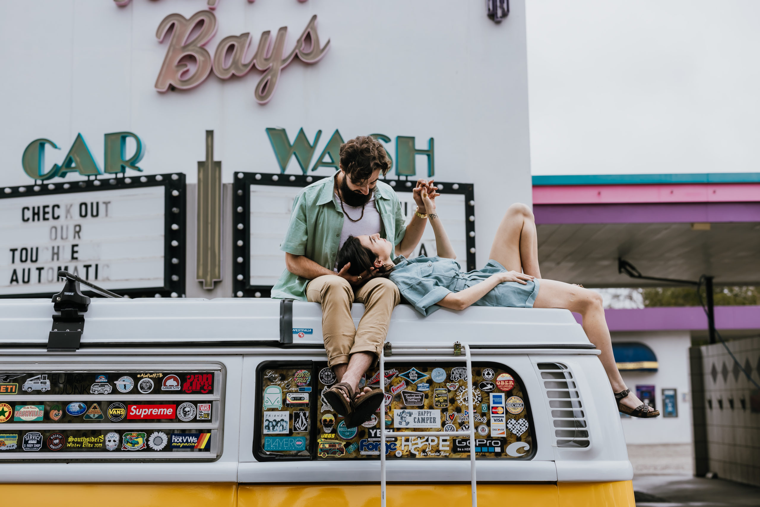 Couple laying on top of vintage, yellow VW bus at retro car wash